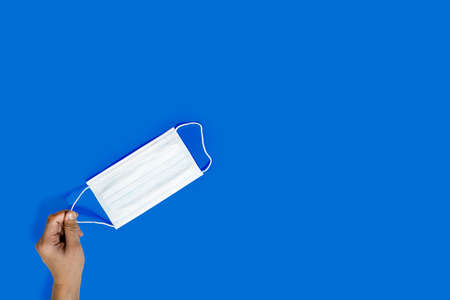Hands holding a mask, Put on a mask to protect against virus, Isolated on blue background. Disease prevention concept.の写真素材