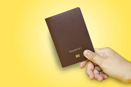 Close up Hand holding passport in brown with yellow background, Passport used for international travel, Isolated on yellow background.の写真素材