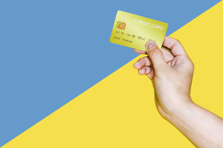 Hand holding a yellow credit card on a blue and yellow background, a hand holding credit card image used in advertising.の写真素材