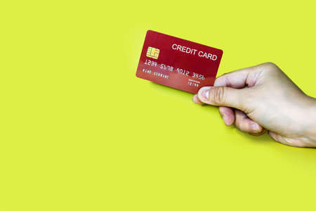Hand holding a red credit card on a yellow background, credit card can be used to pay for goods or services, credit card concept.の写真素材