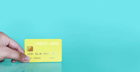 Hand holding a yellow credit card on a blue background, credit card can be used to pay for goods or services, credit card conceptの写真素材
