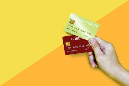 Hand holding a gold and red credit card on a yellow and orange background, holding two credit cards.
