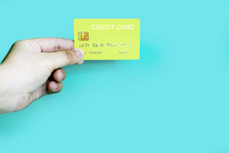 Hand holding a yellow credit card on a blue background, credit card can be used to pay for goods or services, credit card conceptの写真素材