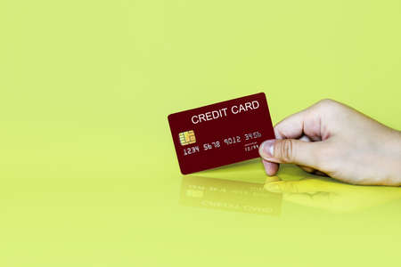 Hand holding a red credit card on a yellow background, credit card can be used to pay for goods or services, credit card concept.の写真素材