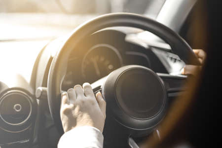 Close-up woman holding the steering wheel of a car, she is driving a car for a trip to the countryside, she is holding the steering wheel to steer the car and intends to drive safely.の写真素材
