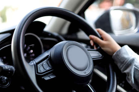 Close-up woman holding the steering wheel of a car, she is driving a car for a trip to the countryside, she is holding the steering wheel to steer the car and intends to drive safely.の写真素材