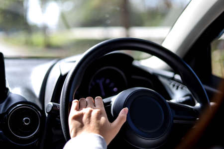 Close-up woman holding the steering wheel of a car, she is driving a car for a trip to the countryside, she is holding the steering wheel to steer the car and intends to drive safely.の写真素材