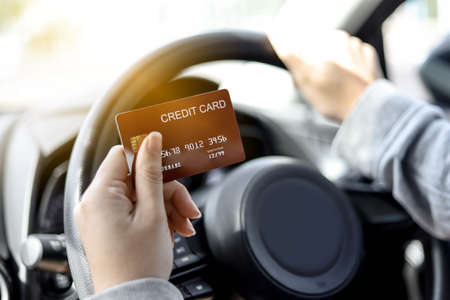 A woman holding a red credit card, she's in the car, she stops filling up the gas station and paying with a red credit card, She was on her way home after going to work. credit card concept.の写真素材
