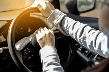 Close-up woman holding a car steering wheel, she is driving a car on a city street, car driving concept.の写真素材