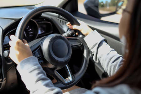 Close-up woman holding a car steering wheel, she is driving a car on a city street, car driving concept.の写真素材
