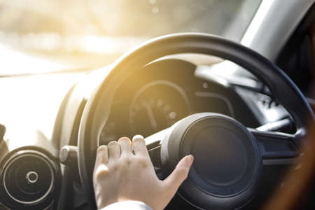 Close-up woman holding a car steering wheel, she is driving a car on a city street, car driving concept.の写真素材