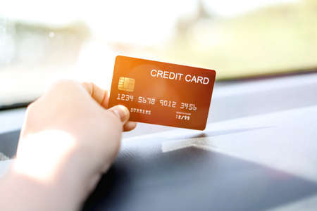 A woman holding a red credit card, she's in the car, she stops filling up the gas station and paying with a red credit card, She was on her way home after going to work. credit card concept.の写真素材