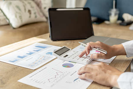 Financial scholars are pressing white calculators to calculate numbers on financial documents to verify the accuracy of company financial data line and pie chart documents. Finance concept.の写真素材