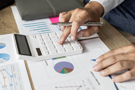 Financial scholars are pressing white calculators to calculate numbers on financial documents to verify the accuracy of company financial data line and pie chart documents. Finance concept.の写真素材