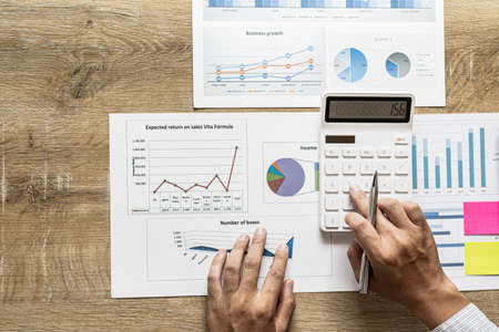 Financial scholars are pressing white calculators to calculate numbers on financial documents to verify the accuracy of company financial data line and pie chart documents. Finance concept.の写真素材