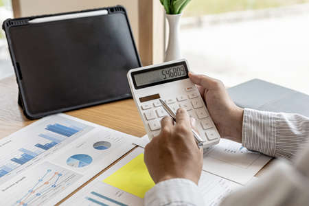 The financial officer presses the white calculator, he calculates the numerical balance on the document to verify the correctness of the balance, the document is displayed in the form of a chart.の写真素材