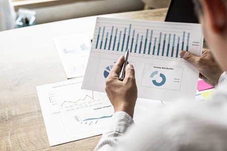 A financial scholar is looking at financial documents to verify the accuracy of company financial information, he is pointing to a document, a line and pie chart. Finance concept.の写真素材