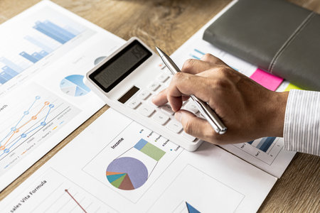 A financial scholar is looking at a financial document to verify the accuracy of a company's financial data, he is pressing a white calculator, a line chart and a pie chart. Finance concept.の写真素材