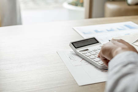 The financier uses a calculator and takes notes in a notebook, he is listing the errors in the financial documents to send to the finance department for review and correction. Financial audit concept.の写真素材