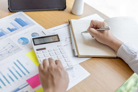 The financial officer presses the calculator to check the information recorded in the book for accuracy before submitting the information in the document to the meeting. Finance concept.の写真素材