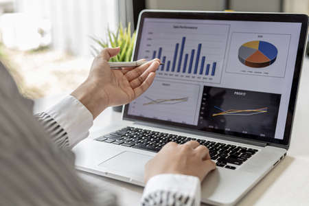 Woman pointing at the laptop screen and documents lying on the table, business woman in black suit is sitting checking information from documents, he is a company executive. Company management conceptの写真素材