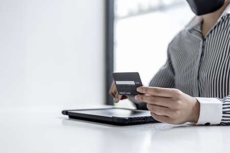 A woman holding a credit card and touching a tablet, she is filling out her credit card information to pay for an order on an online shopping site. Online shopping and credit card payment concept.の写真素材