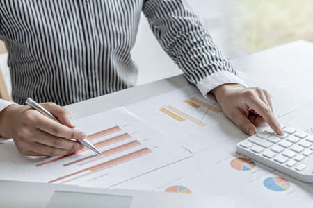 A corporate financier is checking financial documents for the correctness of the financial statements, she is checking the numbers on the documents using a calculator to calculate. Finance concept.の写真素材