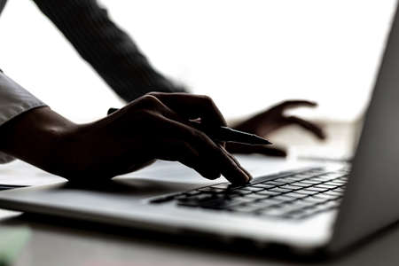 Close-up of business woman's hand silhouette typing on laptop keyboard, she is typing on a laptop...