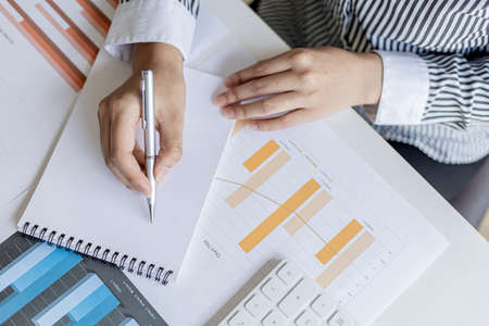 A businesswoman is taking notes in a notebook, she checks company financial documents and she takes corrective reports to the finance manager for correction. Finance concept.の写真素材