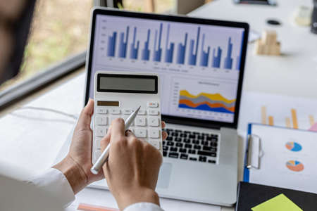 Businesswoman using a calculator to calculate numbers on a company's financial documents, she is...