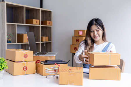 Woman holding parcel boxes to write customer address information before shipping to customers via...