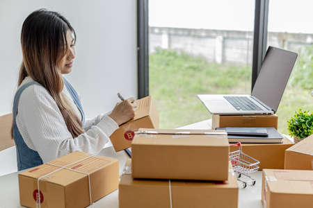 Woman holding parcel boxes to write customer address information before shipping to customers via private transport service, she works online, she sells through website. Online selling concept.の写真素材
