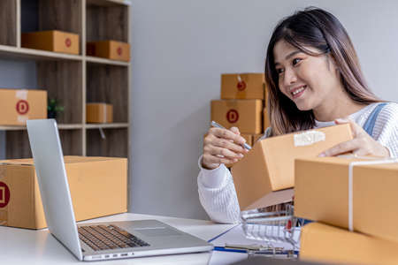 A woman who owns an e-commerce website is video calling chatting with business partners and packing parcels, she is discussing marketing plans to increase sales. Online selling concept.の写真素材