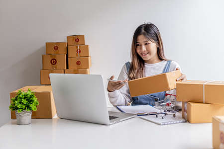 A woman who owns an e-commerce website is video calling chatting with business partners and packing parcels, she is discussing marketing plans to increase sales. Online selling concept.の写真素材