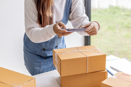 A woman using a smartphone to take pictures in front of parcel boxes, parcel boxes for packing goods, delivering goods through private courier companies. Online selling and online shopping concepts.の写真素材