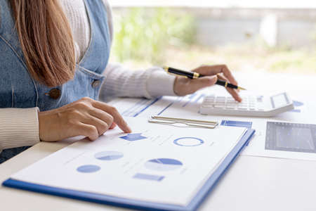 Woman holding a pen pointing to a document on her desk and pressing a calculator, she is checking the numbers on the financial documents prepared by the finance department. Concept of financial audit.の写真素材