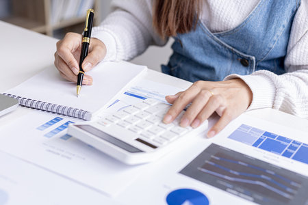Female employee is taking notes and pressing a calculator, she is summarizing the financial documents for a meeting with the head of department, he works in the finance department. Financial concepts.の写真素材