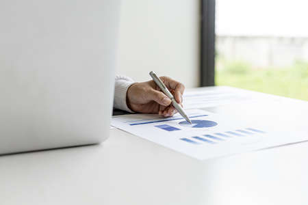 Businesswoman pointing to a pie chart document showing company financial information, she sits in...