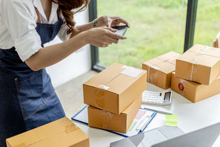 An Asian woman is using a smartphone to take pictures in front of a parcel box for evidence, she...
