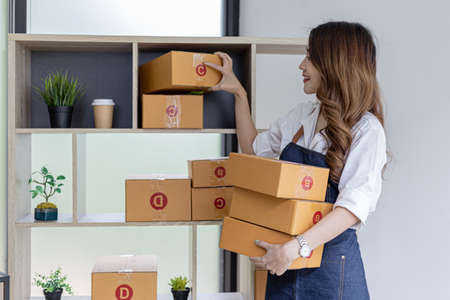 Asian woman puts a packaged parcel on a shelf to prepare it for delivery, owns an online store, she...