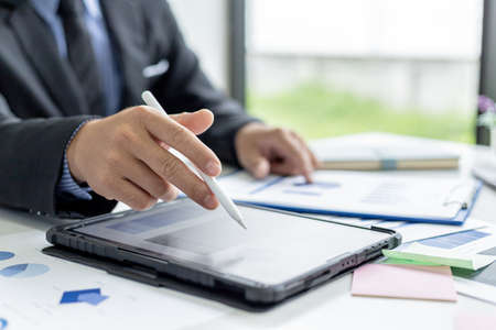 Businessman is using tablet to compare information on financial documents, he is checking company financial documents in office, company financial statements. Concept of financial management.の写真素材