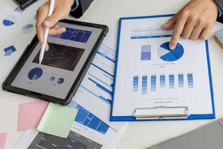 Businessman is using tablet to compare information on financial documents, he is checking company...