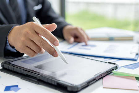 Businessman is using tablet to compare information on financial documents, he is checking company financial documents in office, company financial statements. Concept of financial management.の写真素材