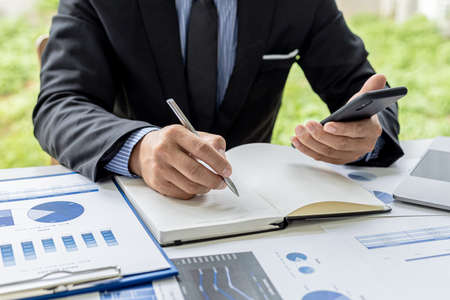 The businessman is taking notes from their mobile phone in a notebook, he owns the company, he is...