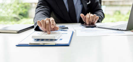 A businessman is pressing a calculator to check numbers on documents, he owns a company, he is checking company financial documents in his office, financial statements. Financial management concept.の写真素材