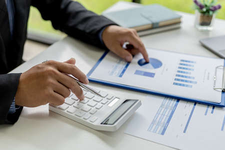 Close-up of a business man using a white calculator, a financial businessman examining the numerical data on a company financial document, He uses a calculator to verify the accuracy of numbers.の写真素材