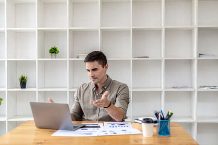 A young businessman is discussing a laptop video conference with a business partner who founded a startup company together, they have a company finance meeting to fix and plan financial arrangements.の写真素材