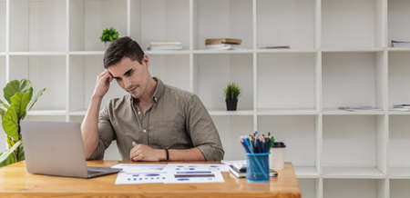 Handsome men are tired from sitting in front of the computer for a long time. Businessmen often suffer from muscle and eye strain due to long hours of work in front of a computer screen.の写真素材