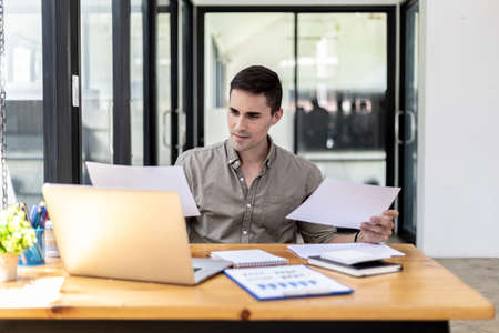 A businessman holding a sales document that the sales department summarizes, he looks displeased when he sees reports of falling sales, he shows signs of stress. Failed sales management concept.の写真素材