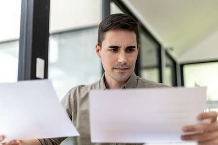 A businessman holding a sales document that the sales department summarizes, he looks displeased when he sees reports of falling sales, he shows signs of stress. Failed sales management concept.の写真素材